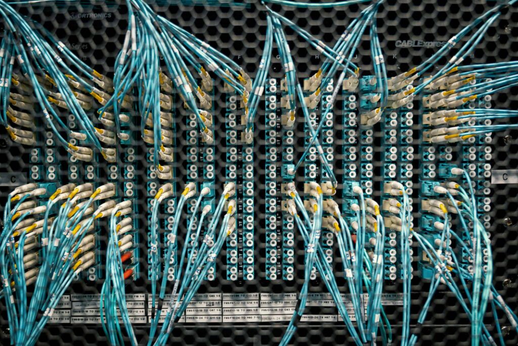 A close-up view of a data center network panel with numerous blue cables connected to various ports, highlighting the complexity and connectivity of data infrastructure.