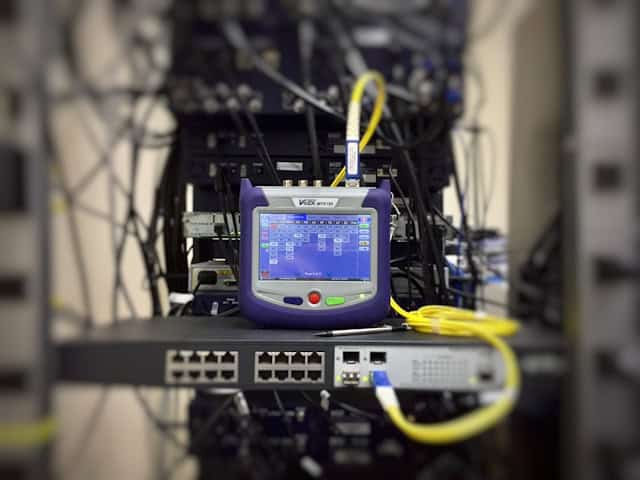 Fiber optic testing equipment connected to a network switch in a business data center, illustrating dark fiber infrastructure setup.
